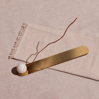 Gold bar and white sphere incense holder on a beige fabric background