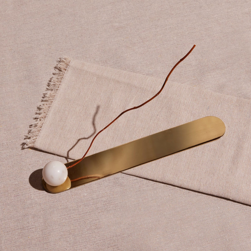 Gold bar and white sphere incense holder on a beige fabric background