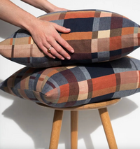 Plaid cushion on a stool with a hand resting on it against a white background