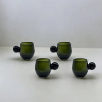 Set of four green glass tumblers with spherical handles on a white background