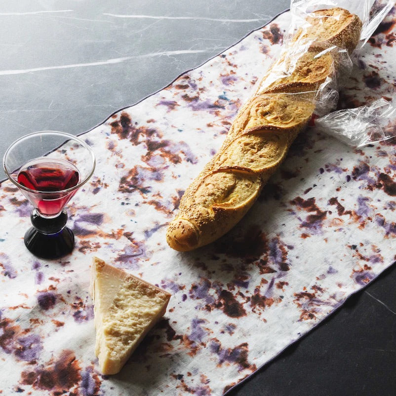 Baguette and cheese on a marble table runner with a glass of red wine.