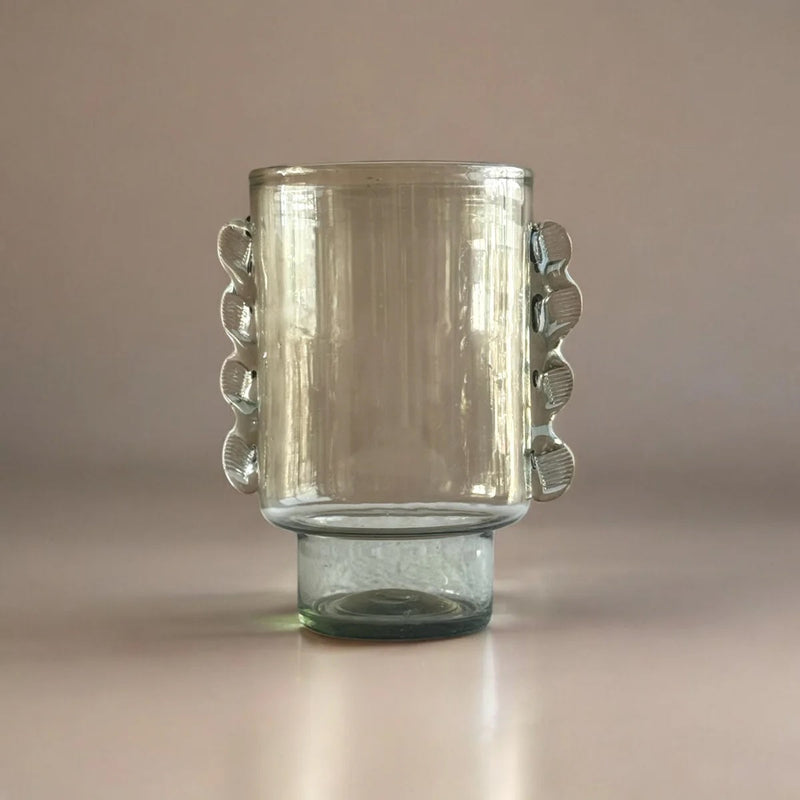 Clear glass mug with textured handles on a beige background