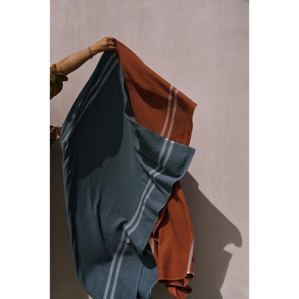 Person holding towels with blue and rust colors against a plain background