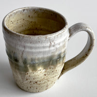 Ceramic mug with light and dark neutral glaze details on a white background