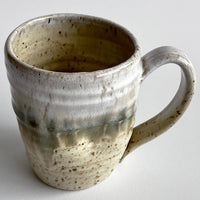 Ceramic mug with light and dark neutral glaze details on a white background