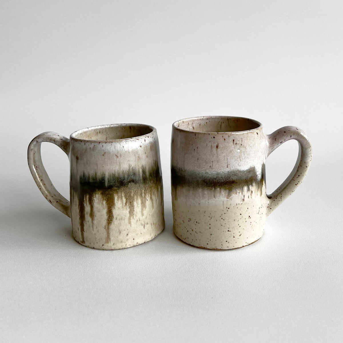 Two ceramic mugs with light and dark neutral glaze details on a white background