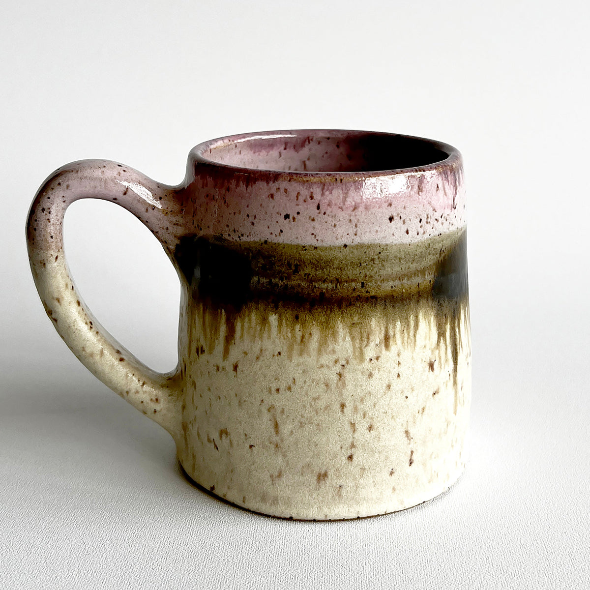 Ceramic mug with light and dark neutral and pink glaze details on a white background