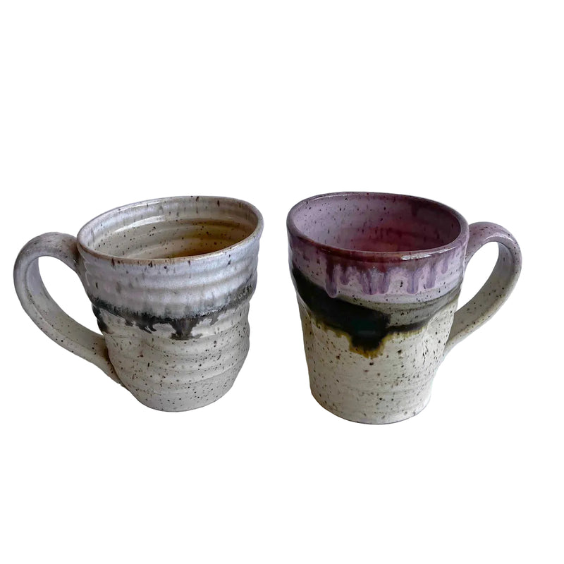 Two ceramic mugs with light and dark neutral and pink glaze details on a white background