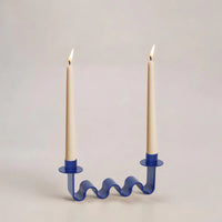 Blue wavy candle holder with two lit candles on a light gray background