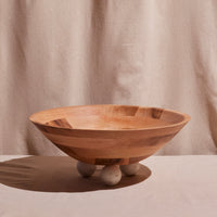 Wooden bowl with three spherical marble feet on a beige background