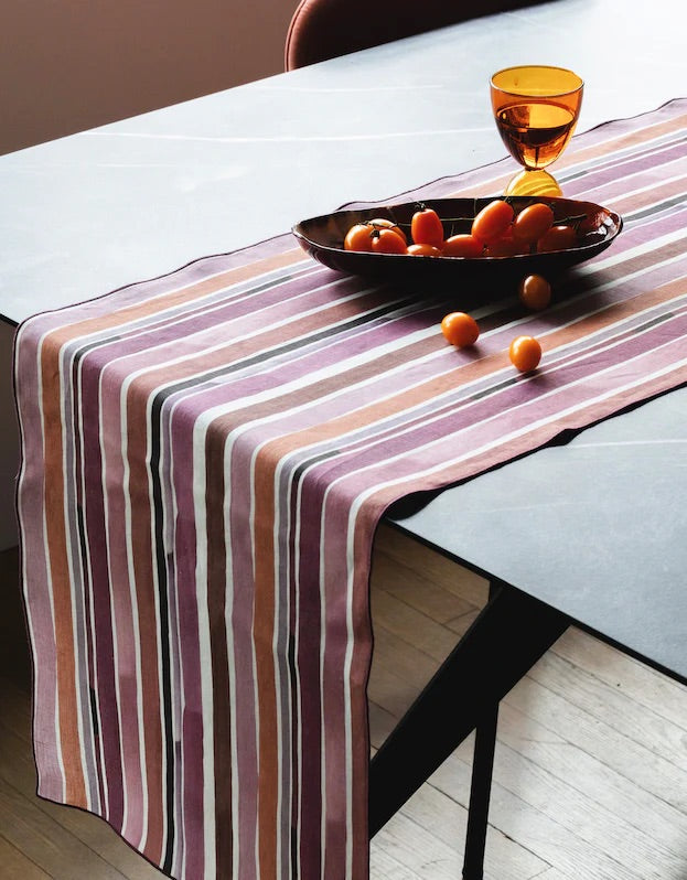 Striped table runner on a dining table with a bowl of oranges.