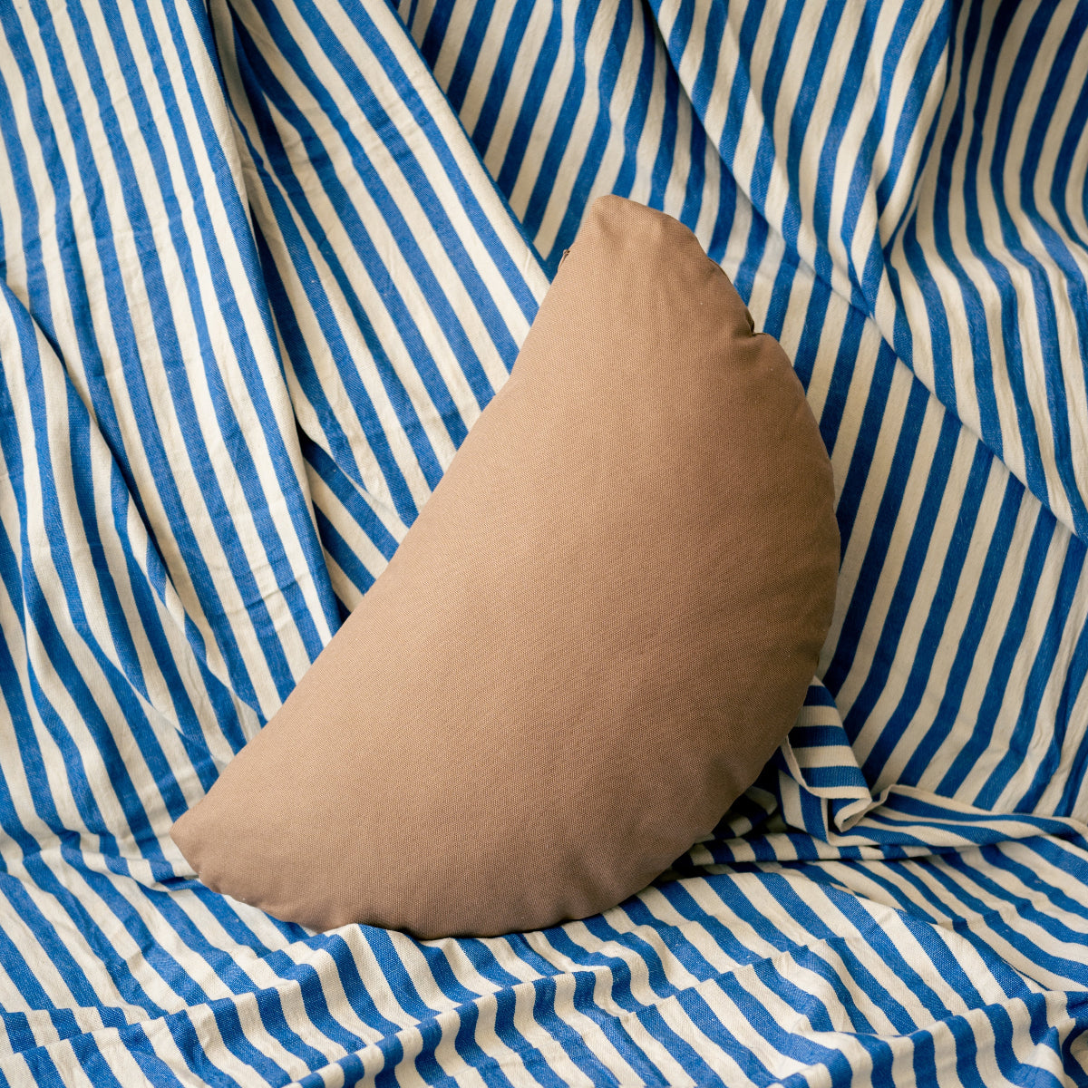Brown half circle pillow on a blue and white striped fabric background