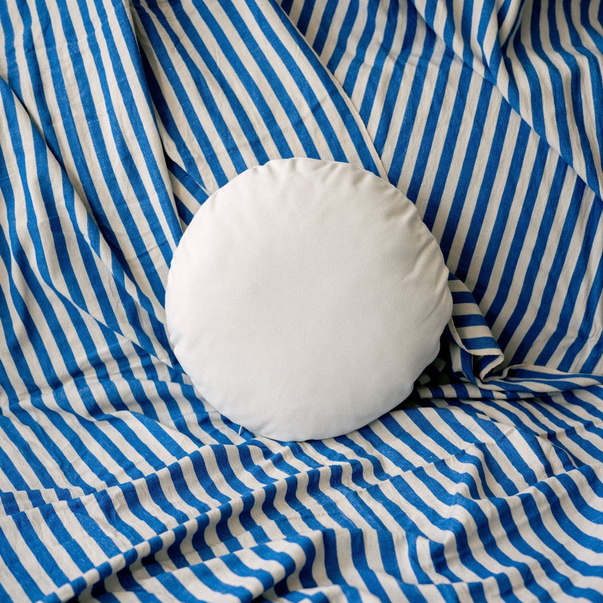 White round pillow on blue and white striped fabric