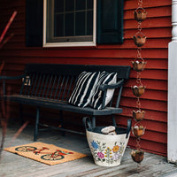 Rain Chain hanging next to a black bench with striped pillow on a wooden porch with red siding.