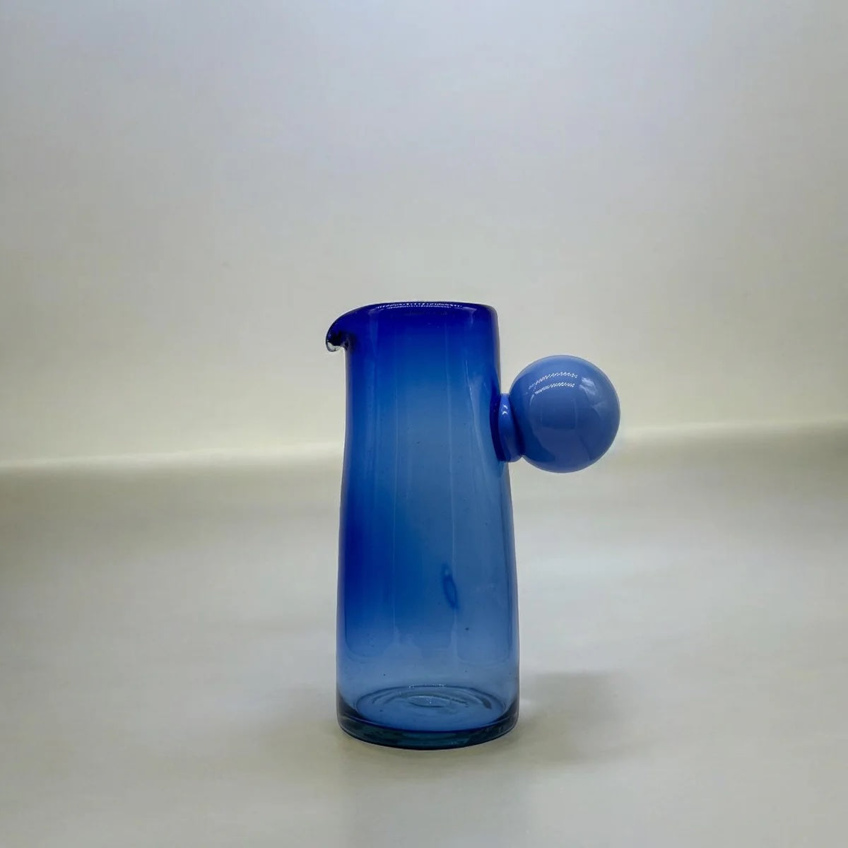Blue glass pitcher with a spherical handle on a white background