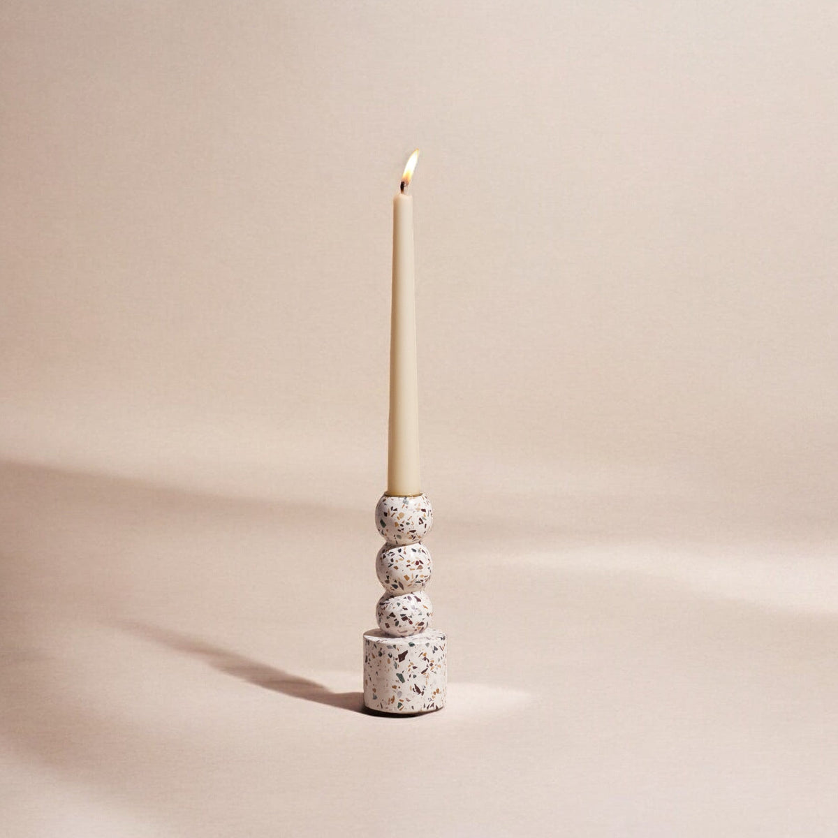 Terrazzo candle holder with a lit candle on a beige background