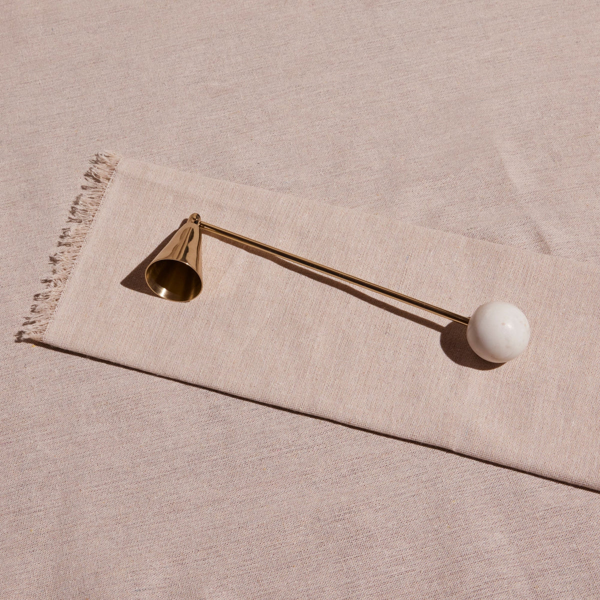 Decorative candle snuffer with a gold bell and white sphere on a beige fabric background