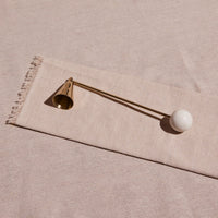 Decorative candle snuffer with a gold bell and white sphere on a beige fabric background