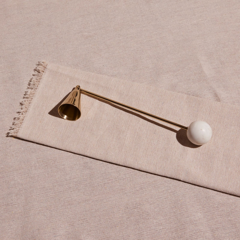 Decorative candle snuffer with a gold bell and white sphere on a beige fabric background