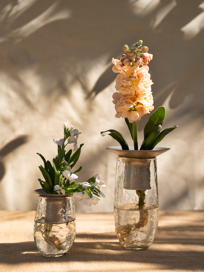 Two glass vases with flowers on a wooden surface with a neutral background