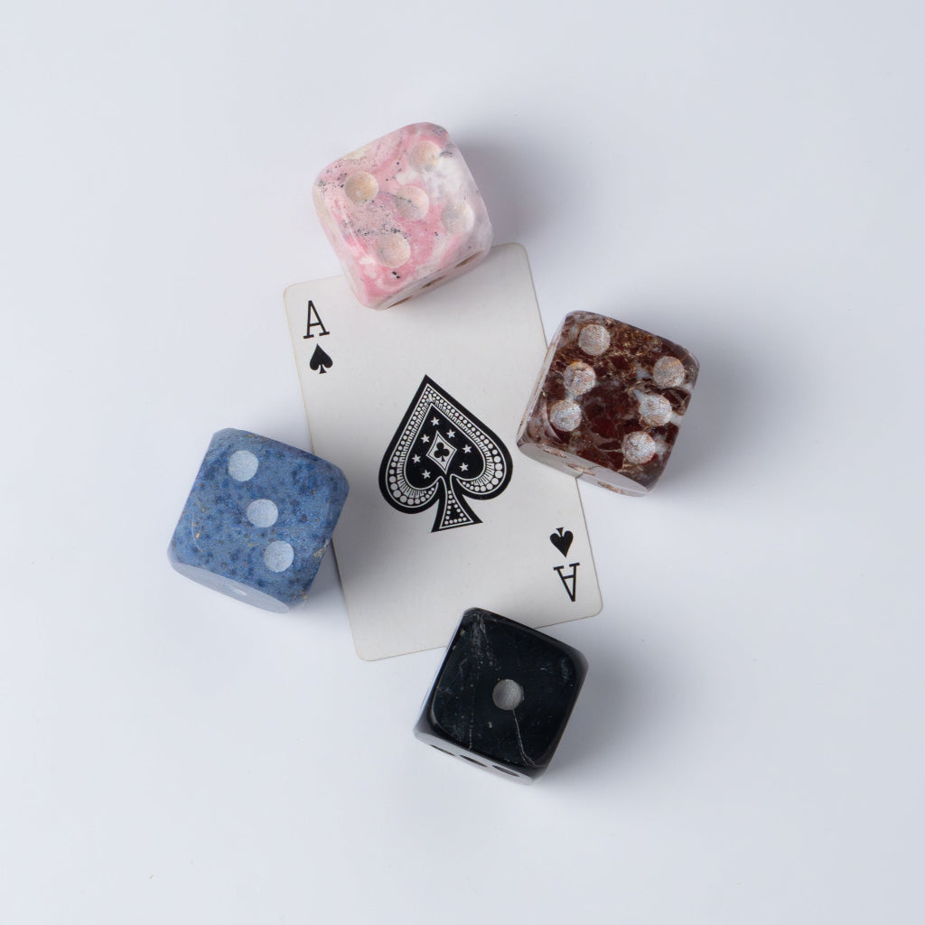 Four colorful stone dice and an Ace playing card on a white surface