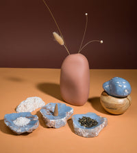 Collection of ceramic and stone items including a vase, bowls, and a small sculpture on an orange surface with a brown background.