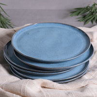 Stack of blue ceramic plates on a beige cloth with green plants in the background