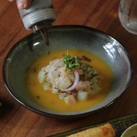 Pasta plate with seafood and vegetables being drizzled with a sauce on a wooden table
