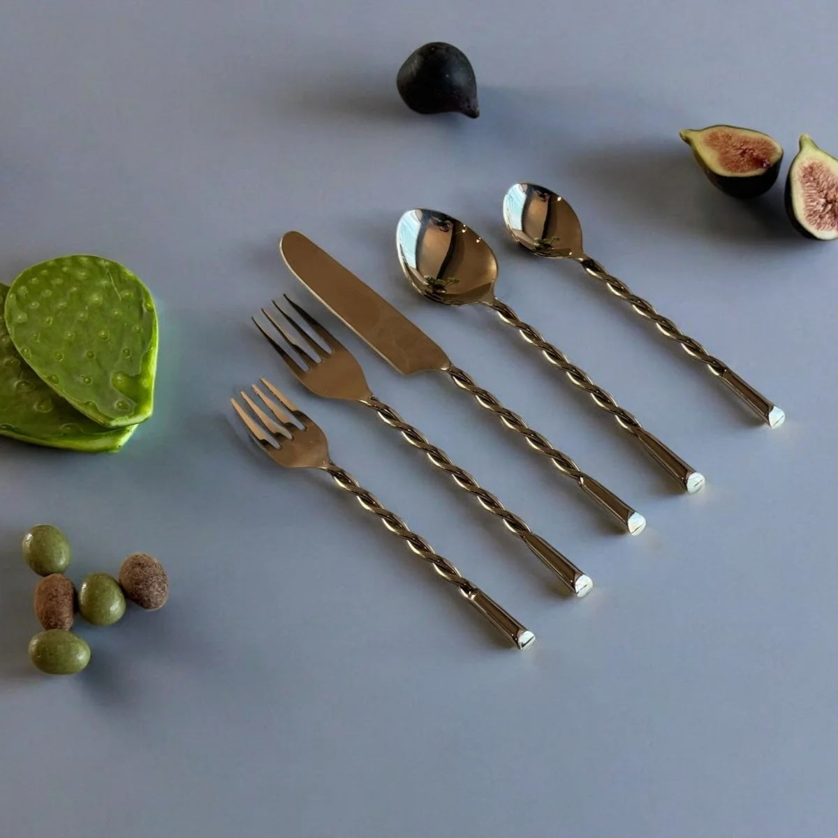 Silver cutlery set with figs, green leaves, and small fruits on a gray surface