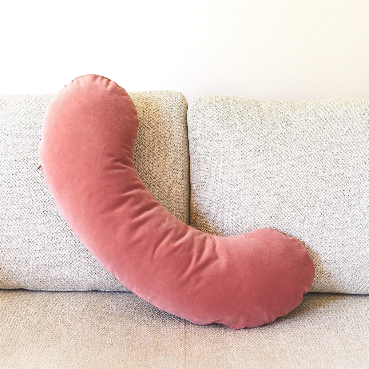 Pink U-shaped pillow on a beige sofa