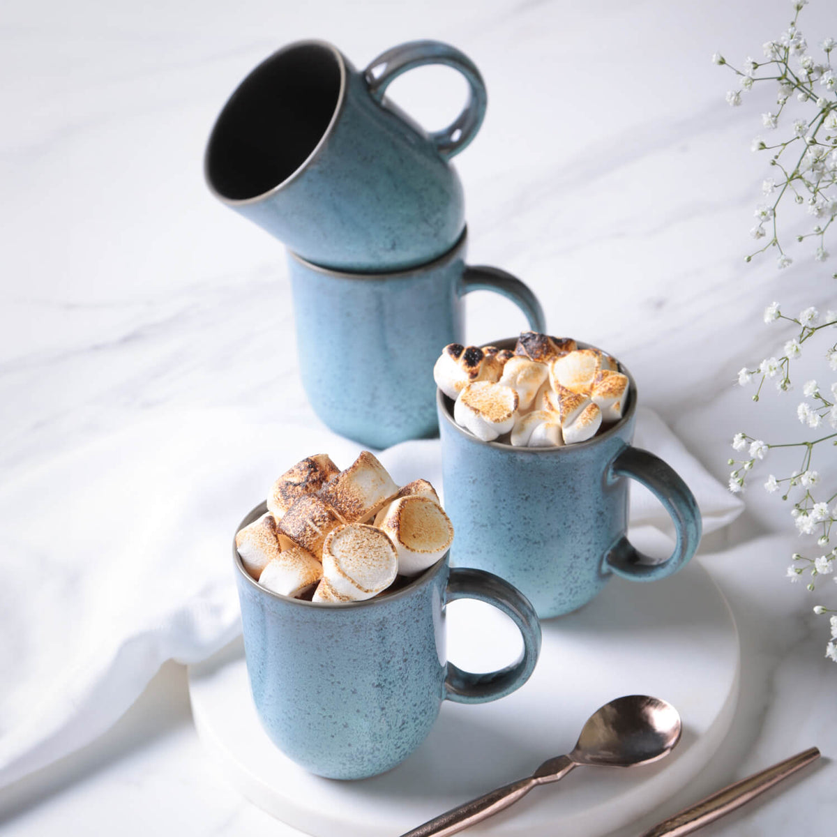 Blue ceramic mugs filled with toasted marshmallows on a white surface.