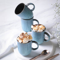 Blue ceramic mugs filled with toasted marshmallows on a white surface.