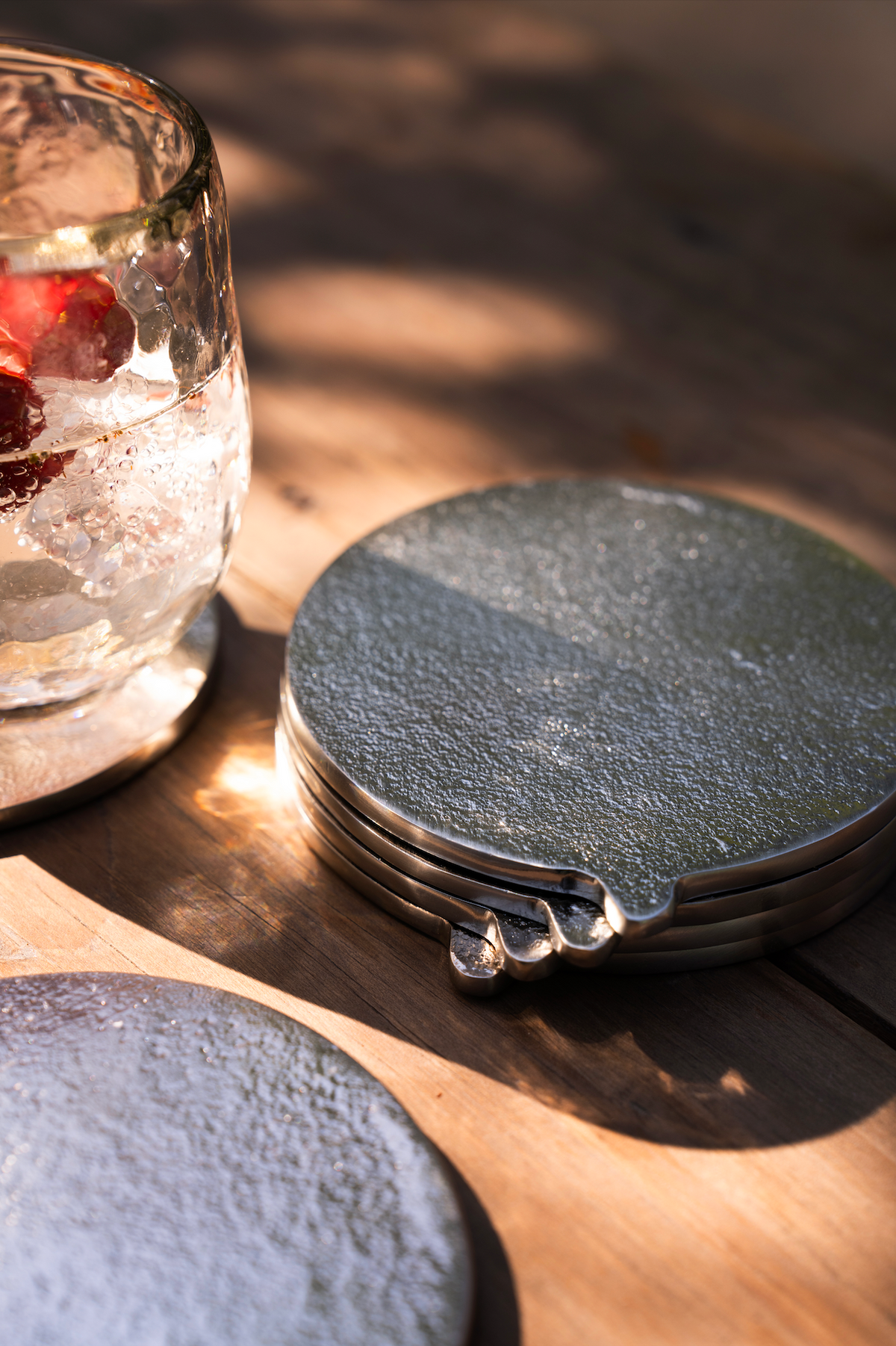 Set of round silver coasters on a wooden surface with a glass of water and berries.