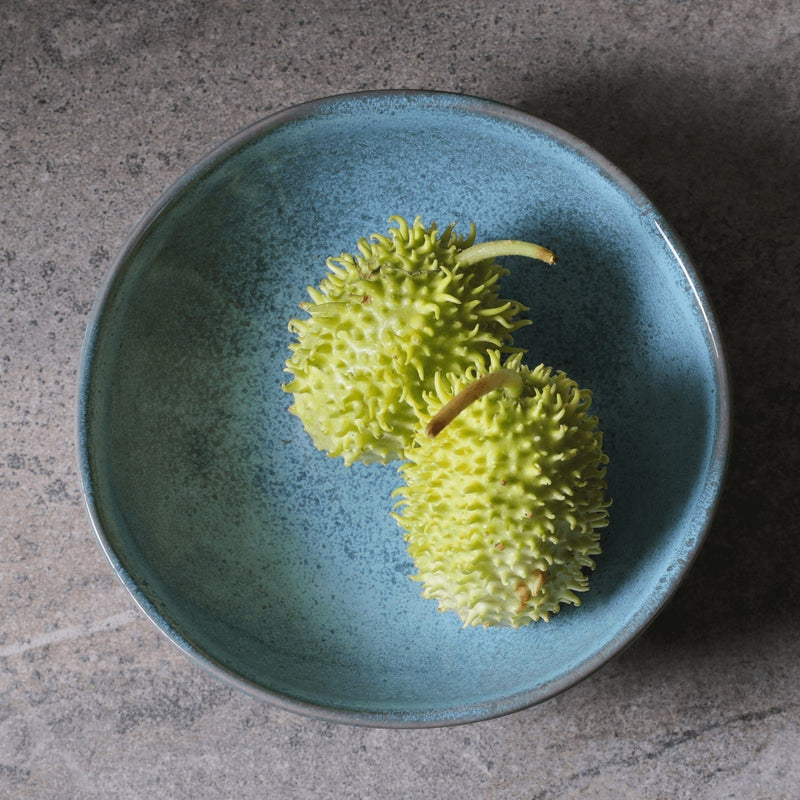 Two green fruits in a blue ceramic bowl on a gray surface