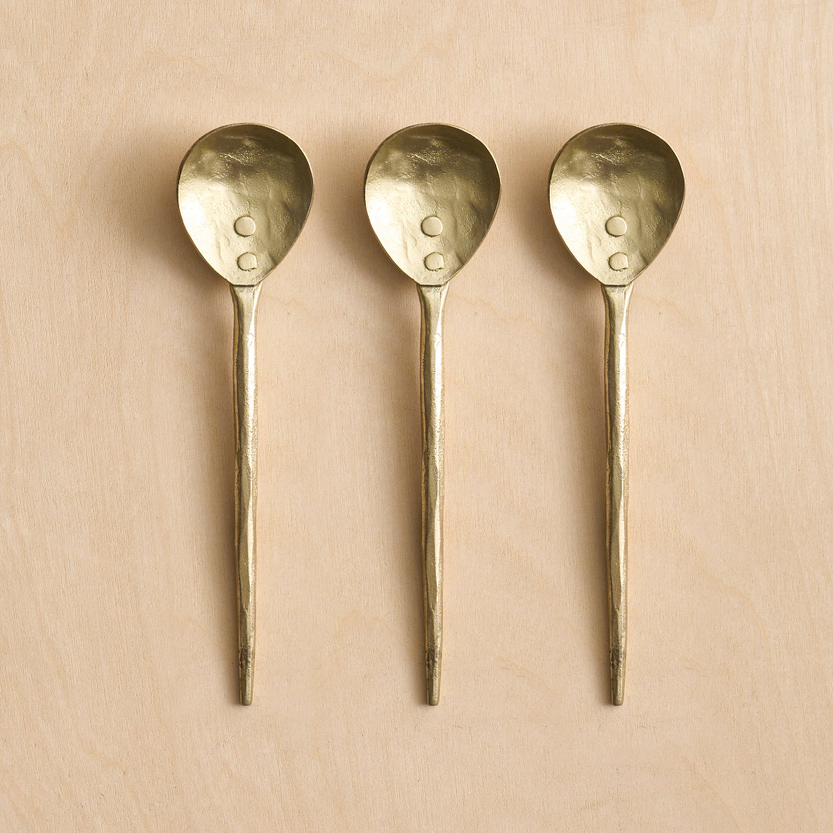 Three small brass spoons on a wooden surface