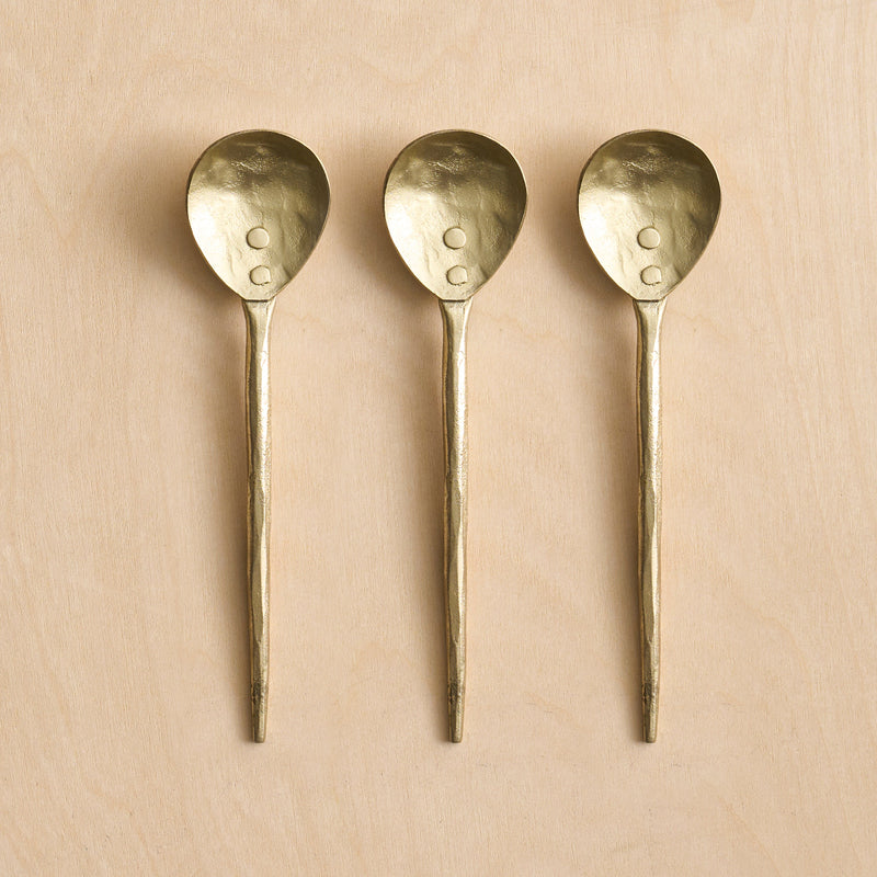 Three small brass spoons on a wooden surface