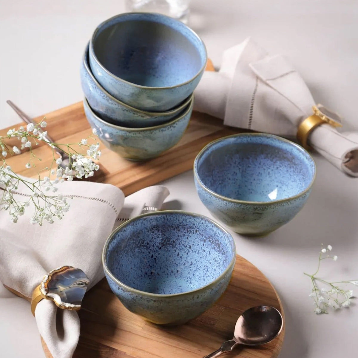 Set of blue ceramic bowls on a wooden tray with white napkins and silver spoons.
