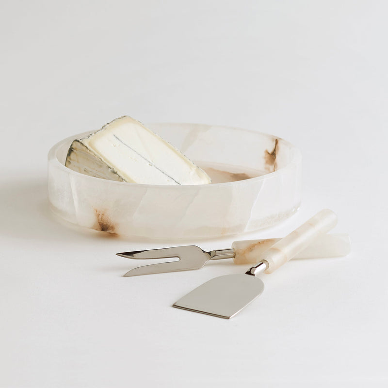 White alabaster cheese tray with silver and alabaster cheese tools on a light gray background
