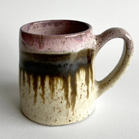 Ceramic mug with light and dark neutral and pink glaze details on a white background