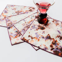 Set of four patterned cocktail napkins with a glass of red liquid on a white background
