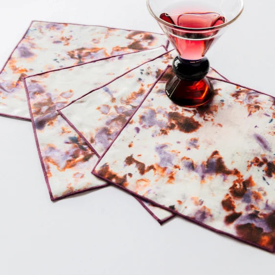 Set of four patterned cocktail napkins with a glass of red liquid on a white background