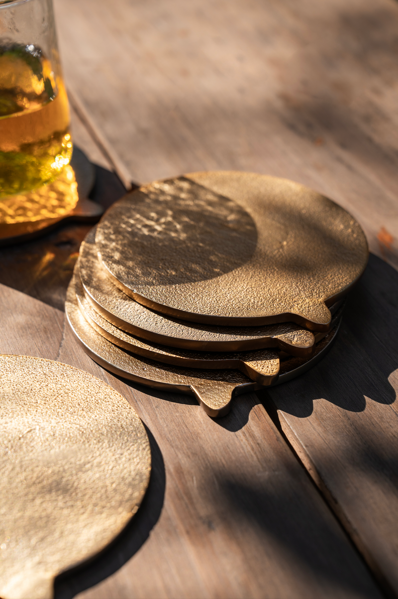 Set of brass coasters on a wooden surface with a glass of amber liquid in the background.