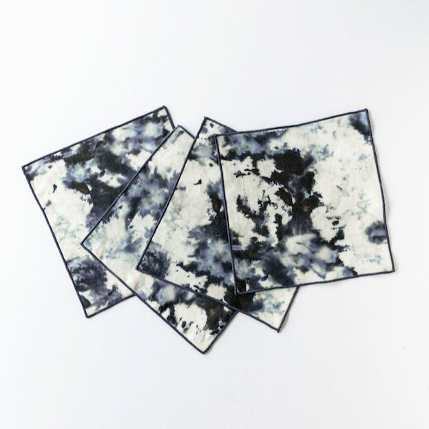 Four square cocktail napkins with a tie-dye pattern in black and white on a white background.