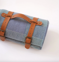 Roll-up fabric mat with brown leather straps on a white background