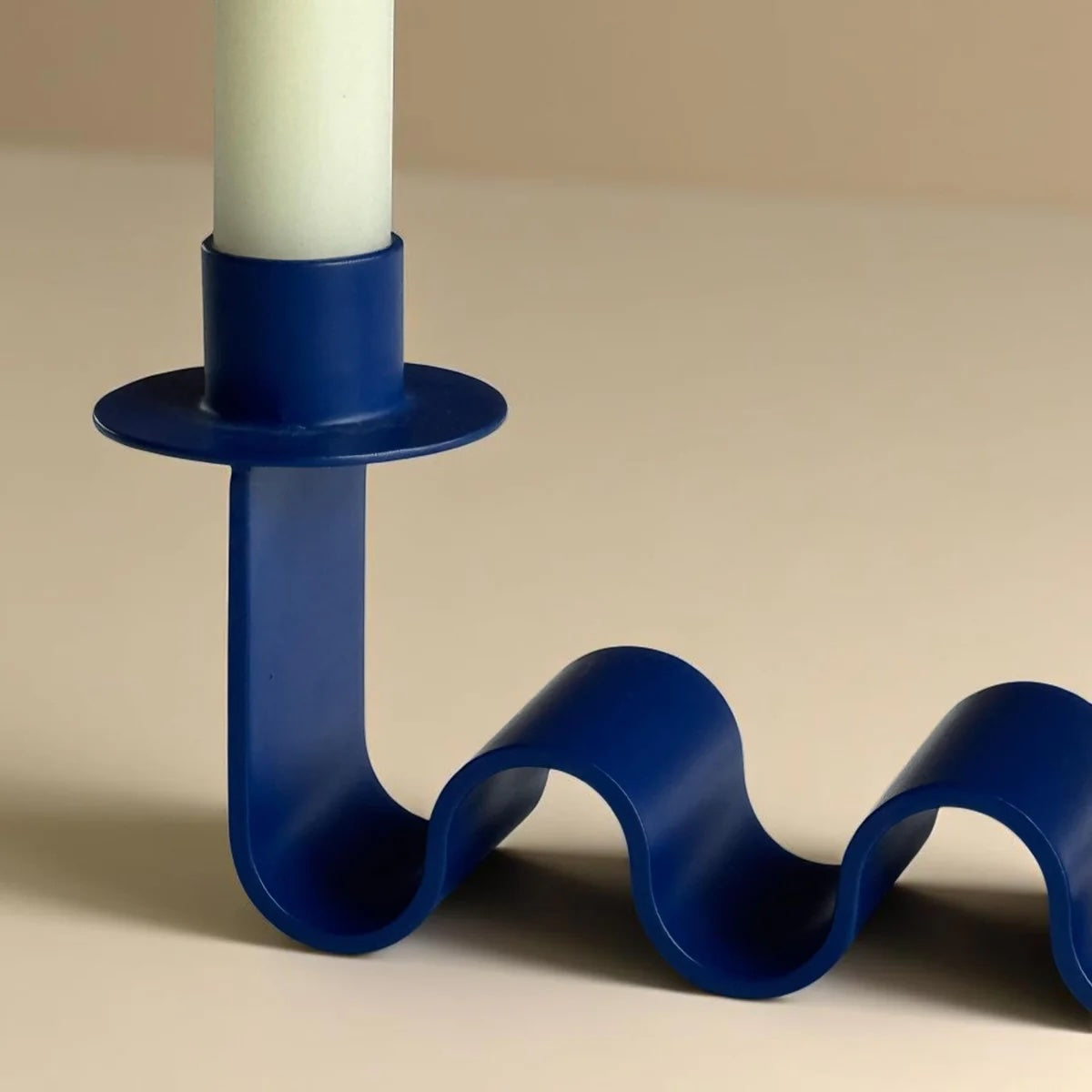 Close up of a blue wavy candle holder with a white candle on a beige background
