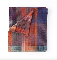 Folded blanket with a checkered pattern in purple, orange, and blue on a white background