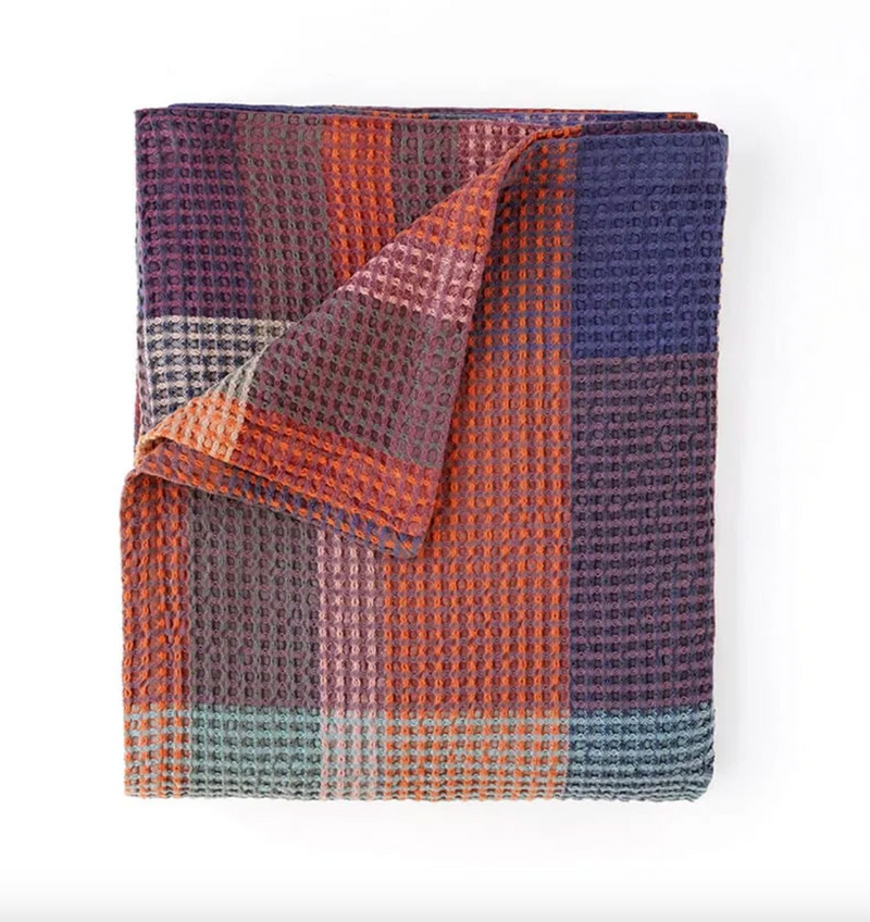 Folded blanket with a checkered pattern in purple, orange, and blue on a white background