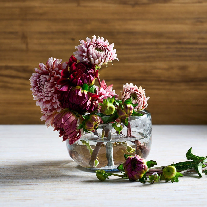 Clear glass vase with pink and red flowers on a wooden surface