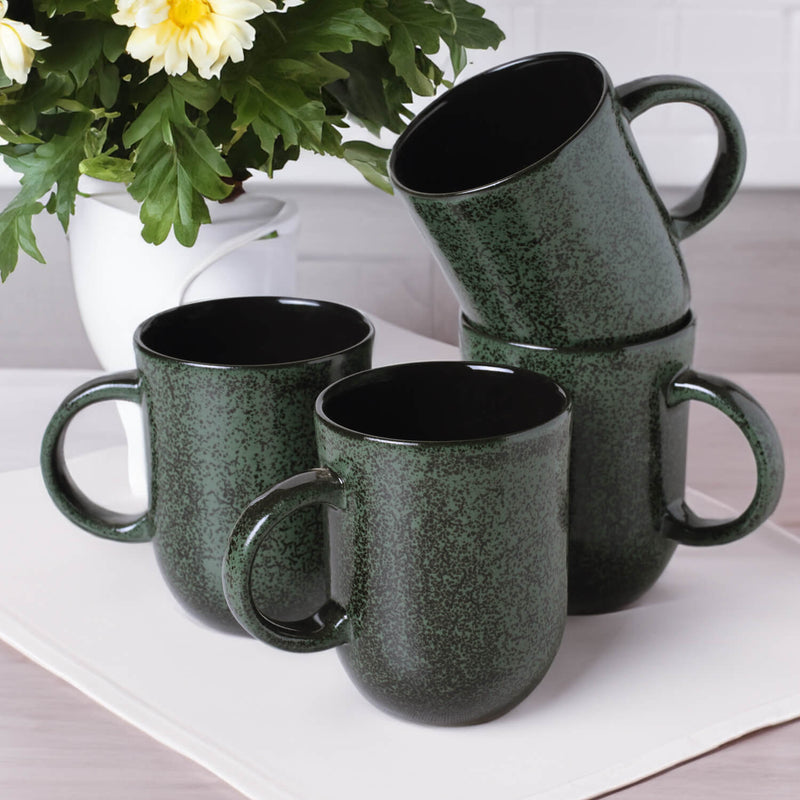 Set of 4 green mugs on a white surface with a plant in the background
