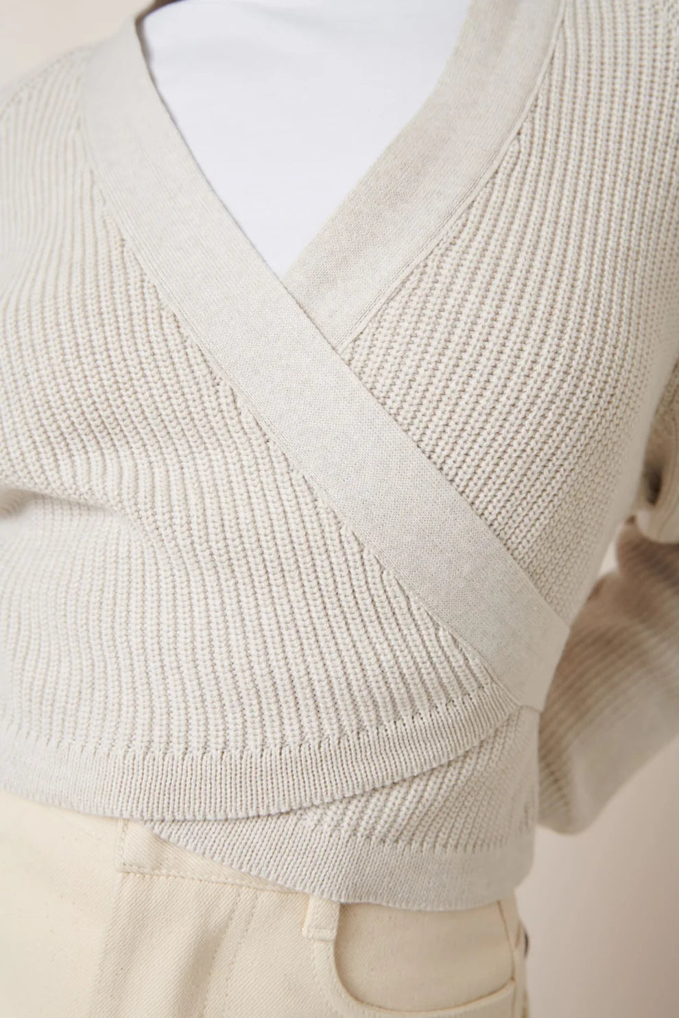 Beige knitted sweater with criss-cross design on a person against a neutral background